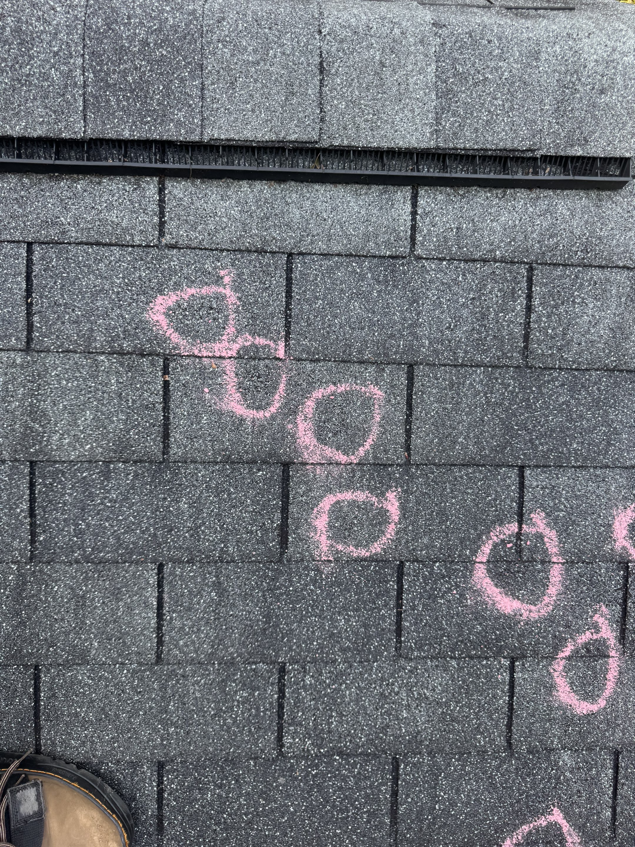 Close-up of dark gray asphalt shingles with pink chalk circles drawn around individual hail strike marks. Each circle is documented damage that goes into the insurance scope.
